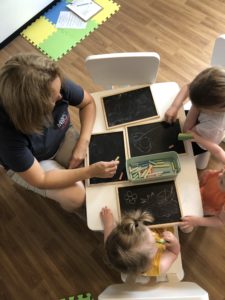 volunteer and small children draw on chalkboards at a table