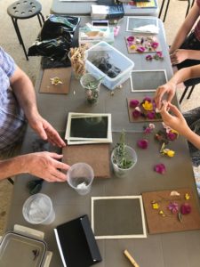 artist and participant hands on a table arranging petals on glass