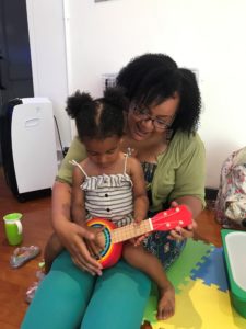 little girl sits on her mum's lap playing a rainbow guitar