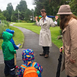 children in bright raincoats talk to two detectives in the park