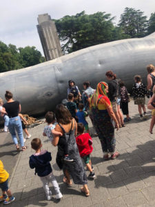 lots of family audience gather outside The Whale, it's summer so the children are in shorts and tshirts and parents in dungarees